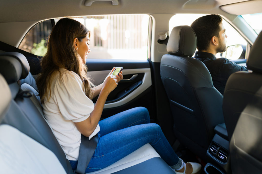 Uber Accident Lawyer Burbank, CA - Side view of an attractive latin woman sitting on the car back seat and using a ride share app on her smartphone