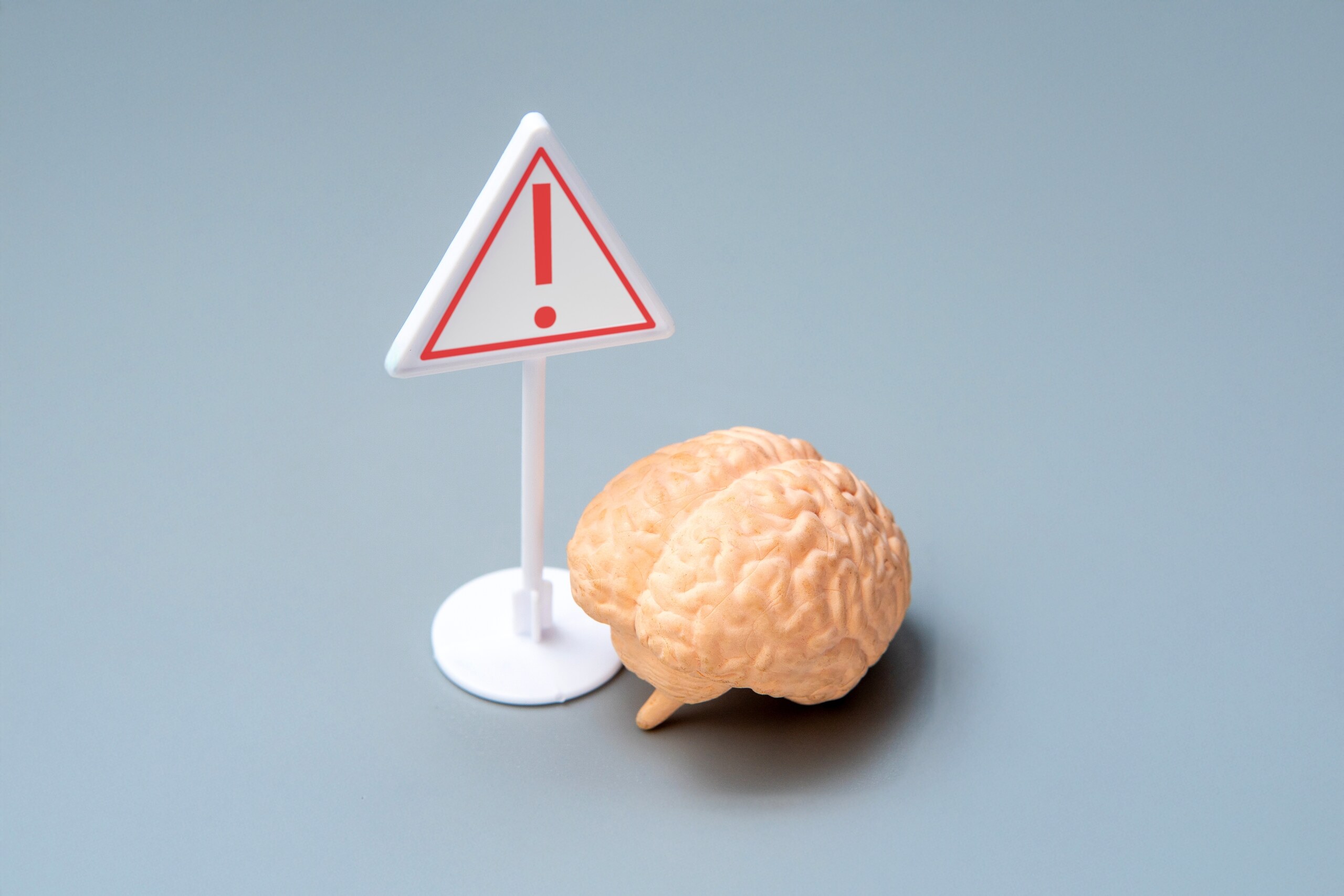 A red warning sign stands beside a brain model to illustrate the risks of an Anaheim brain injury.