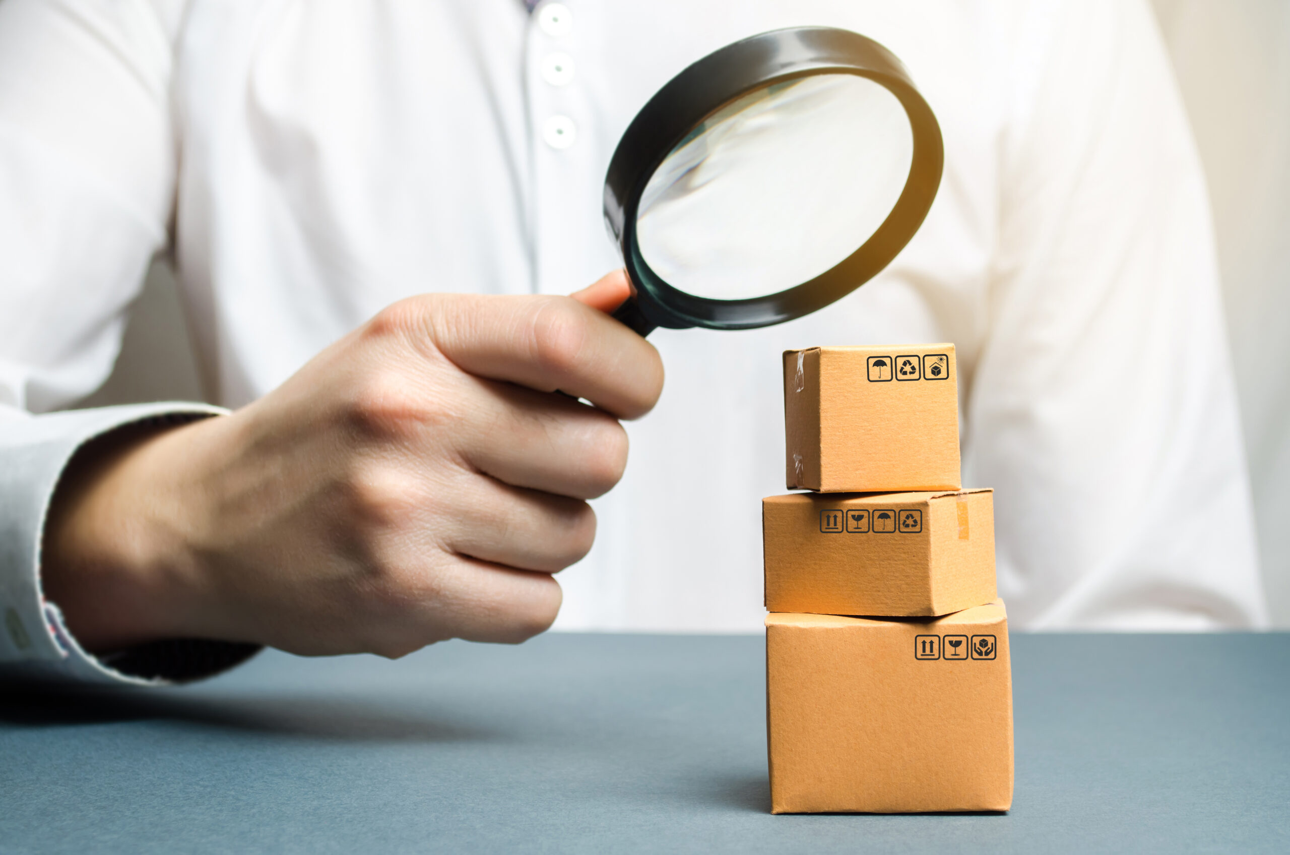 Hand inspecting cardboard shipping boxes with a magnifying glass to demonstrate product inspection handled by Anaheim product liability lawyers.