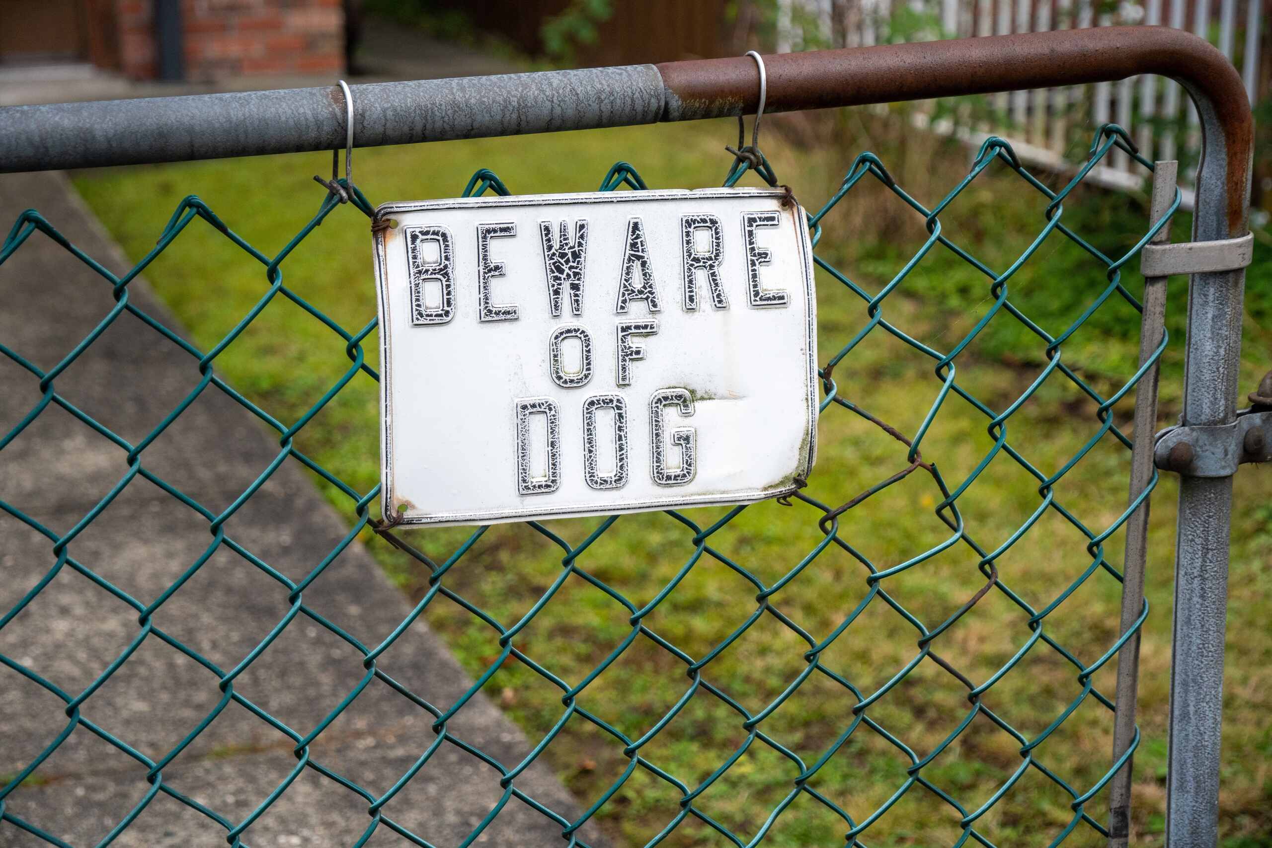 A beware of dog sign hangs on a metal chain link fence, key evidence considered by Los Angeles dog bite attorneys.