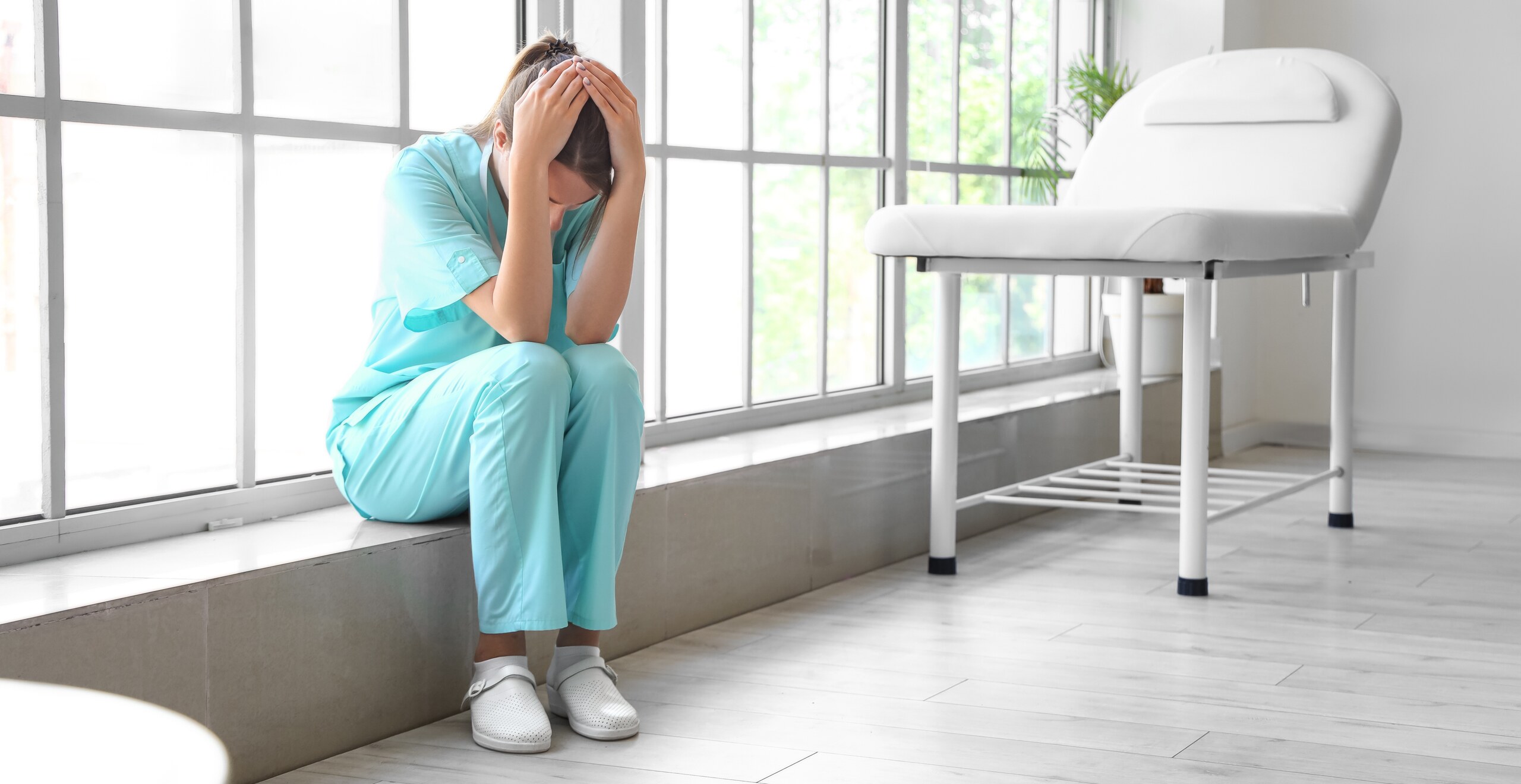 A distressed medical worker sits on a window ledge in a setting where Los Angeles wrongful death attorneys handle malpractice claims.