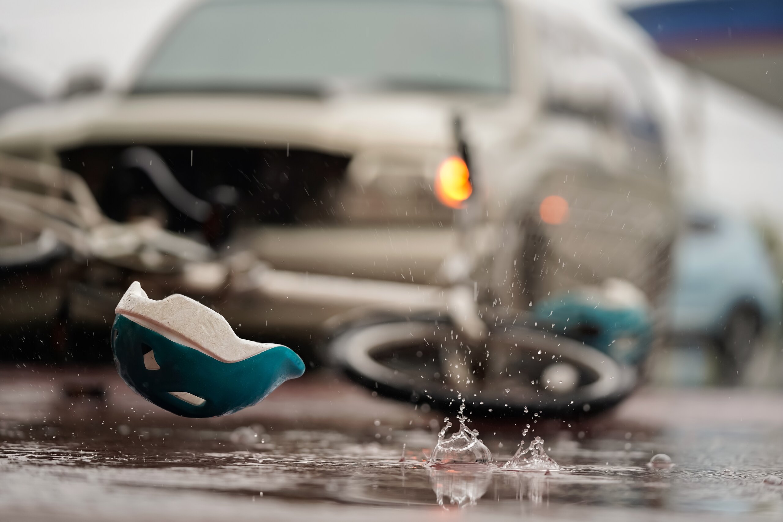 A childs helmet lies on wet pavement near a fallen bicycle and a car with its headlights on.