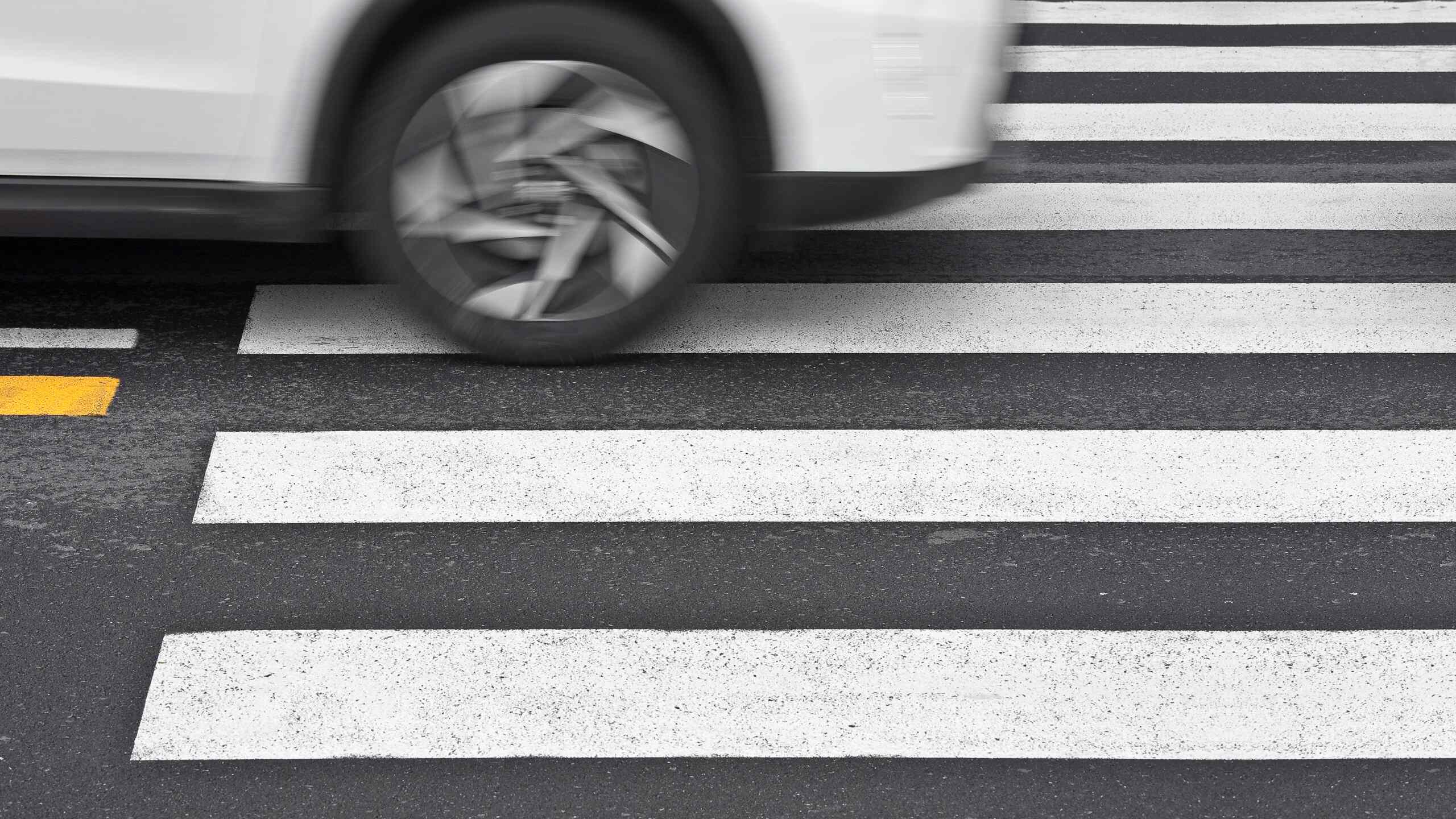 A white car driving over a pedestrian crosswalk.