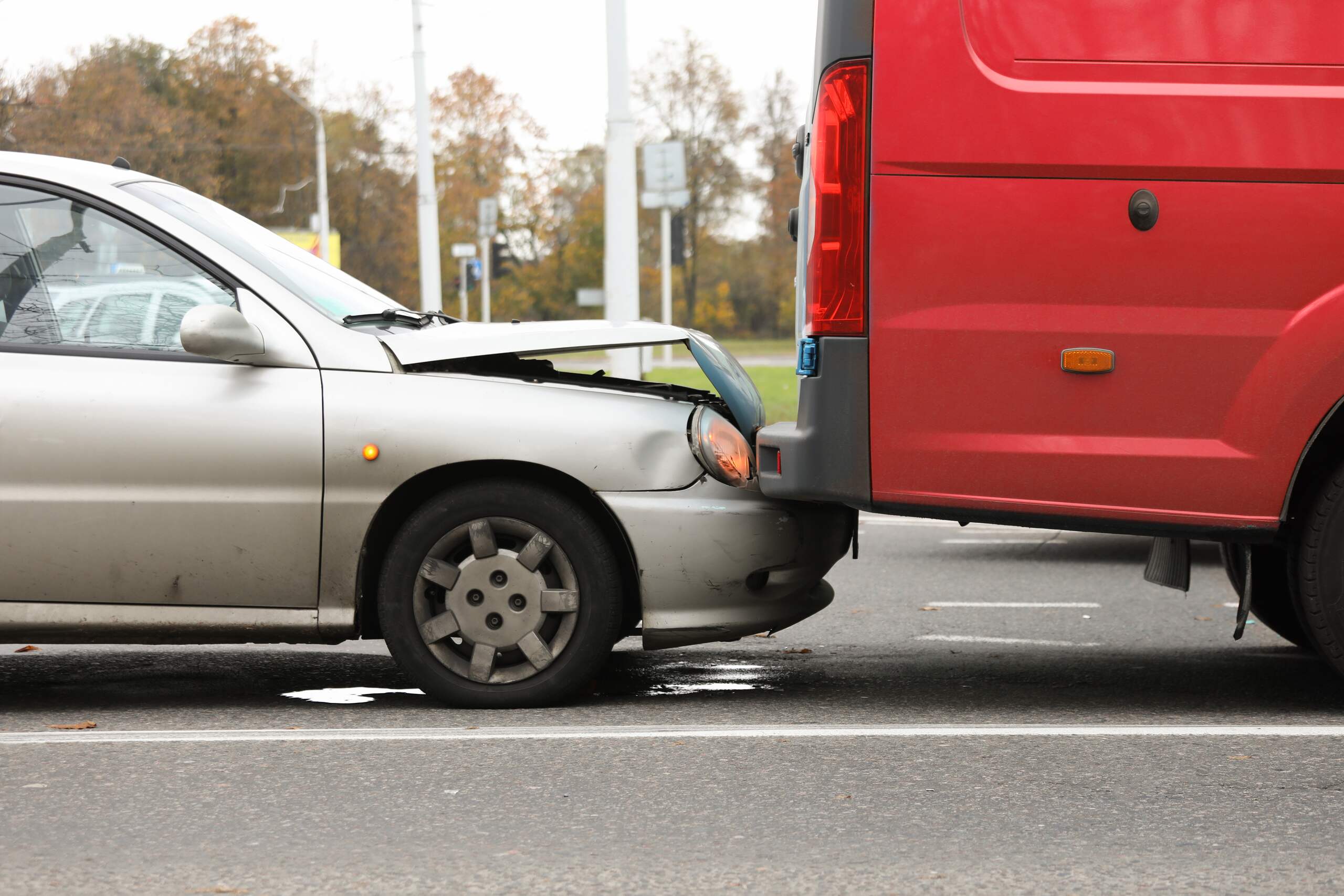 A silver sedan has rear-ended a red van, resulting in a crumpled hood on the sedan.