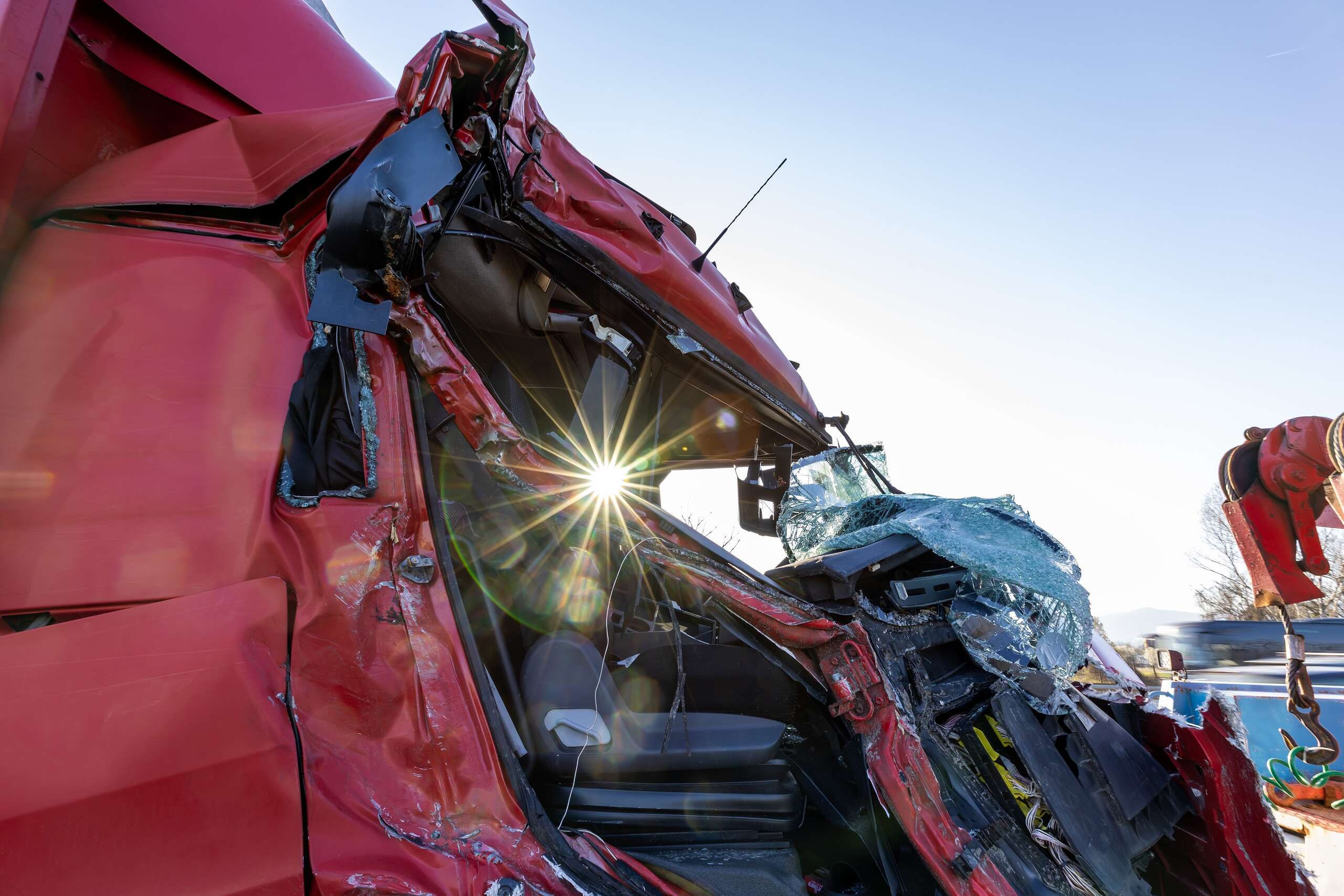 A heavily damaged red semi-truck cab with a shattered windshield.